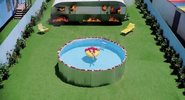 a woman is floating in a swimming pool in front of a trailer on fire