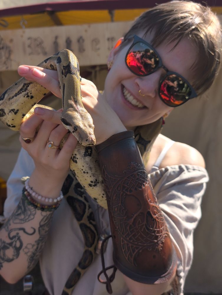 Photo of me holding a snake (boa imperator). I'm wearing sunglasses, a creme blouse, golden jewelry and a brown leather armguard. the snake is wearing nothing but his beautiful light yellow skin with black spots, he looks a little like an adorable banana. 