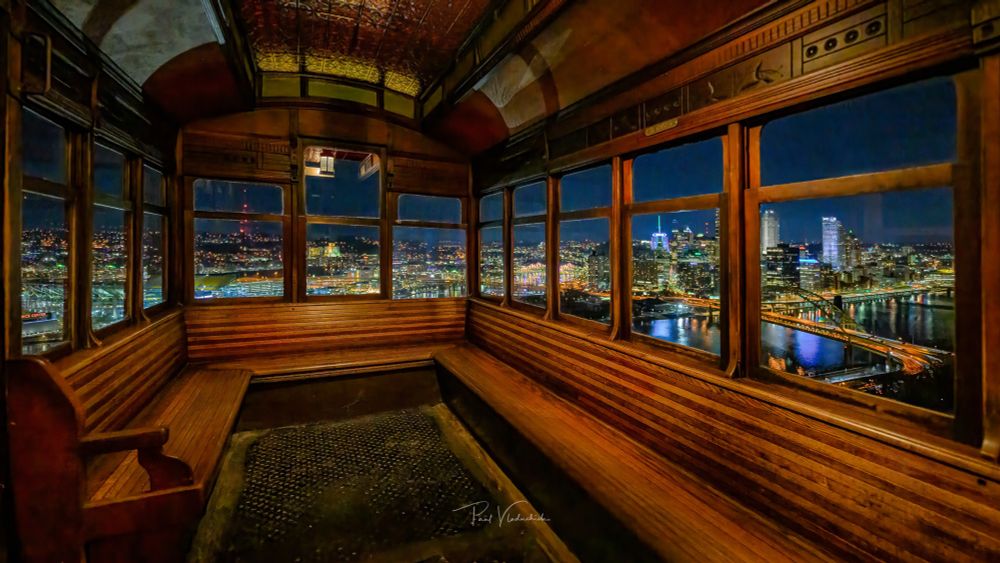 A photograph of the inside of the Duquesne Incline at night. The city is visible through the windows 