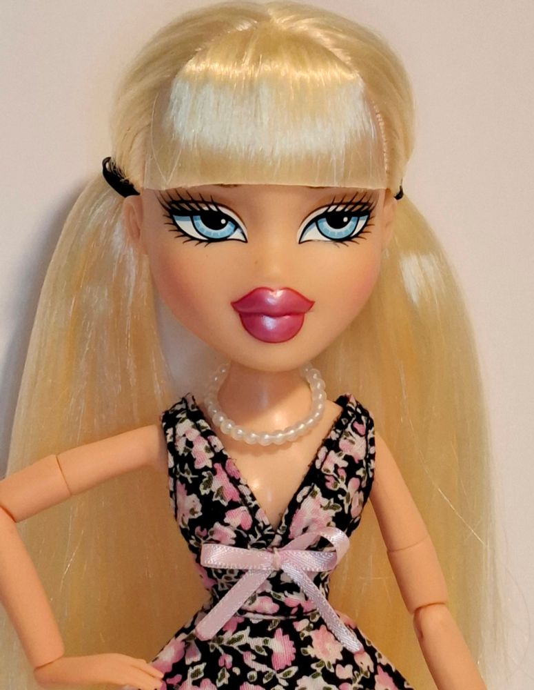 Blonde Bratz doll with black and pink floral dress woth pink lace and a pink bow. Close up photo from waist up.