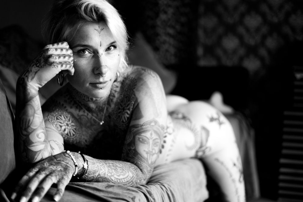 Naked tattooed woman with beautiful eyes laying on a couch in black and white