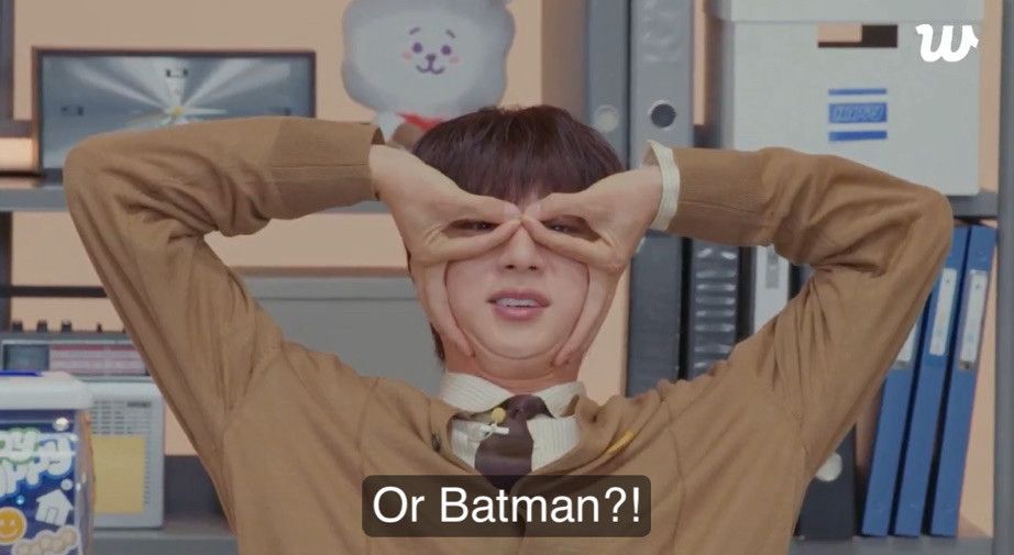 BTS’ Seokjin creating a Batman mask with his hands, covering his eyes with a mask created with his fingers.  