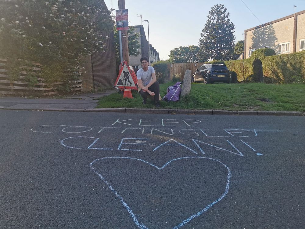 A wide shot of Matt posing with a bag of litter picked rubbish and a message in chalk: "Keep Cottingley Clean!".