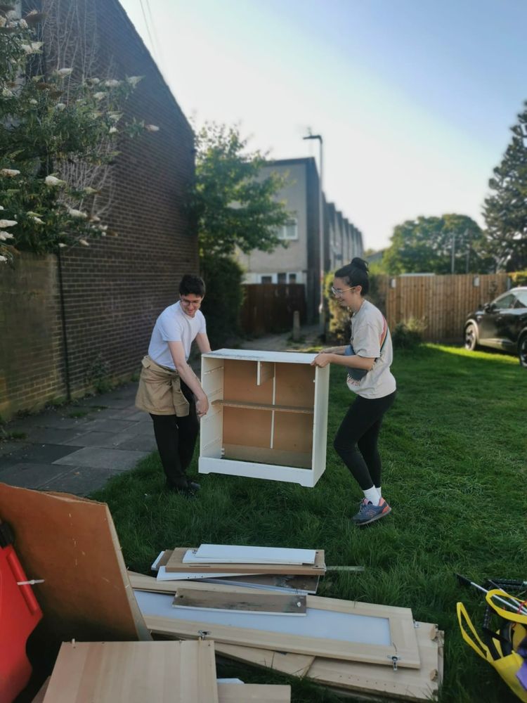 A photo of Matt and Cristiana moving a fly-tipped chest of drawers off of green space.
