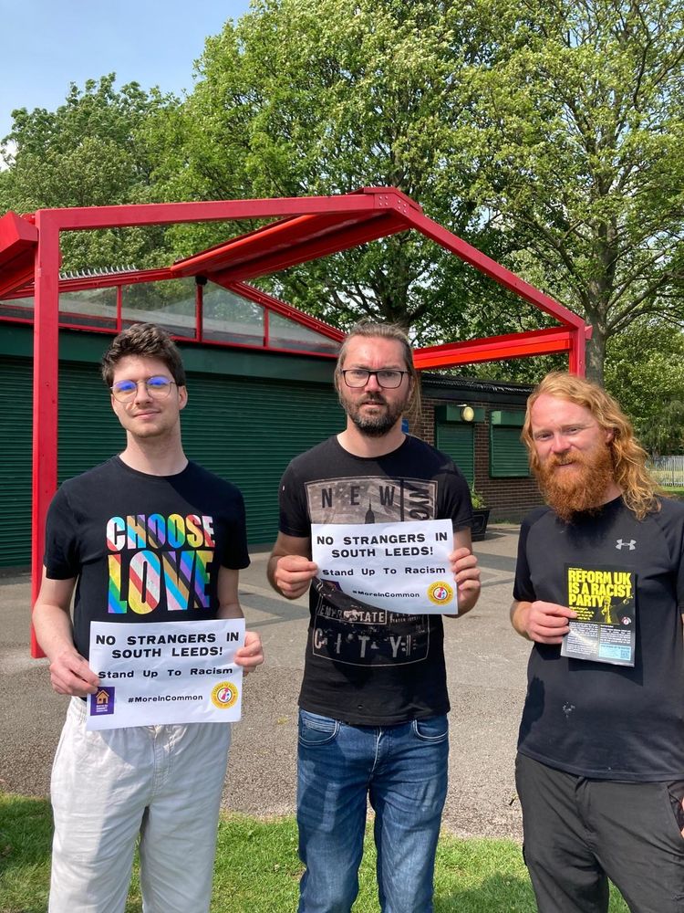 A photo of Matt, James, and Chris holding signs saying "No Strangers in South Leeds! Stand Up To Racism". 