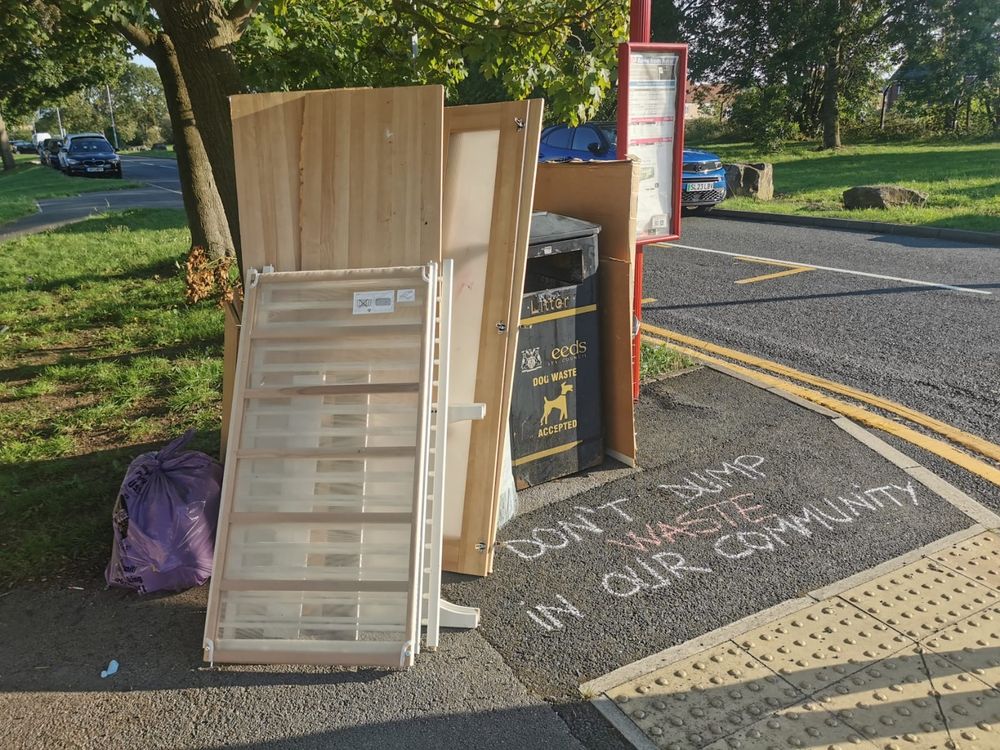 A haul of fly-tipping by a bin, with a chalked message: "Don't dump waste in our community"
