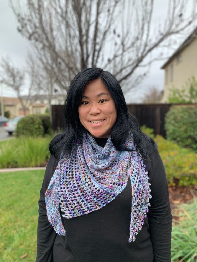 A woman with black hair and a black shirt wears a bluish-purple, lace shawl.