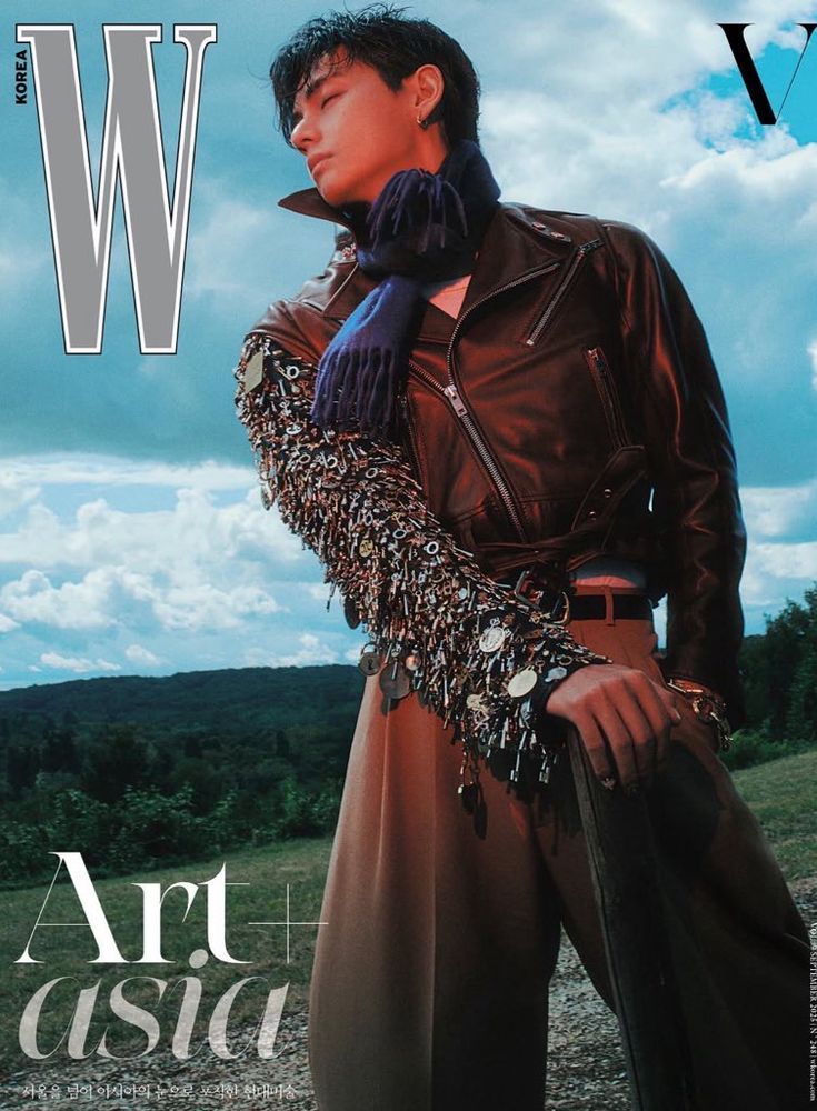 W magazine cover with tae standing looking wistfully to the side with his hand resting on a post, dressed in a leather jacket and scarf with one arm bedazzled in what looks like jewelers and metal pieces 