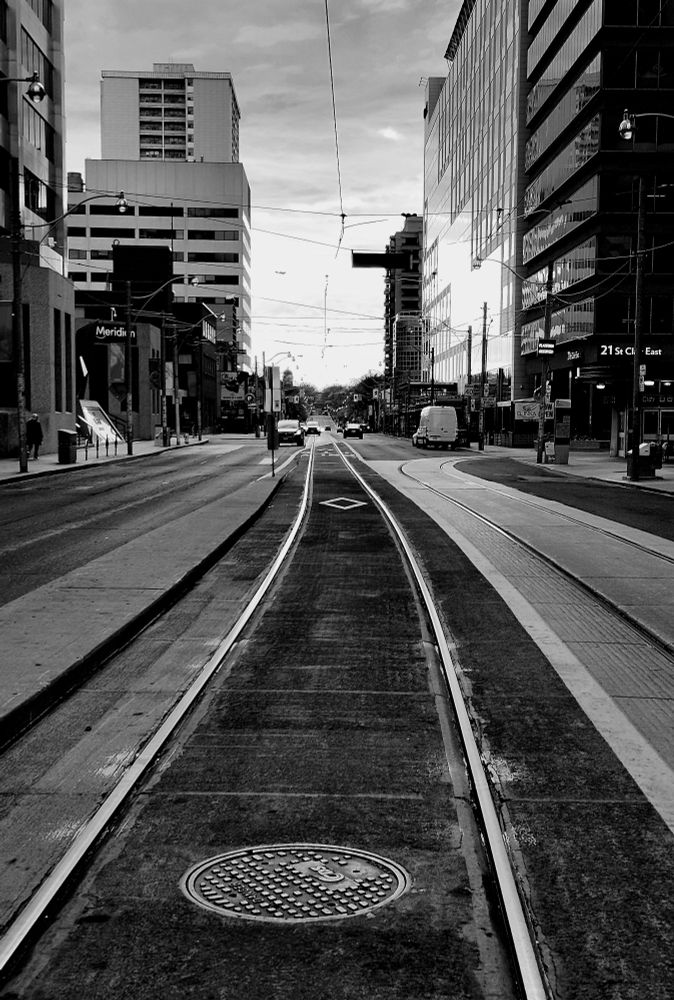 Bordered by high-rise buildings, lines of streetcar tracks on a wide, painted road stretch into the light of a distant horizon.