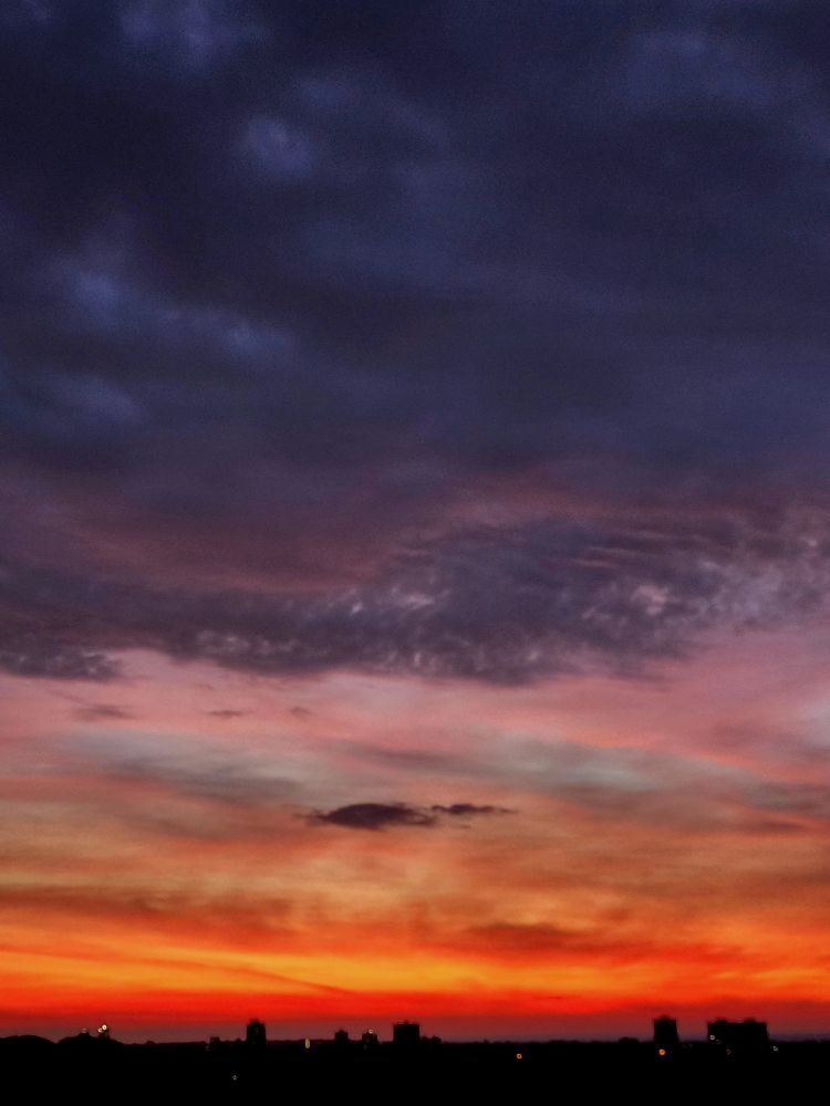 Dawn breaks over the city skyline with streaks of gold and orange under purple clouds. 