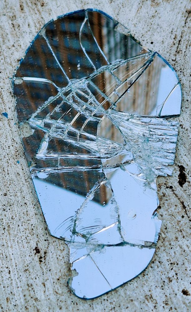A piece of shattered mirror on a sidewalk brokenly reflects the inverted image of high-rise building.