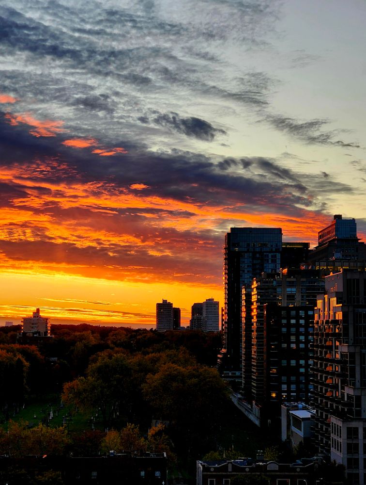 The setting sun paints the cloudy sky over a cityscape shades of golden yellow and bright orange.