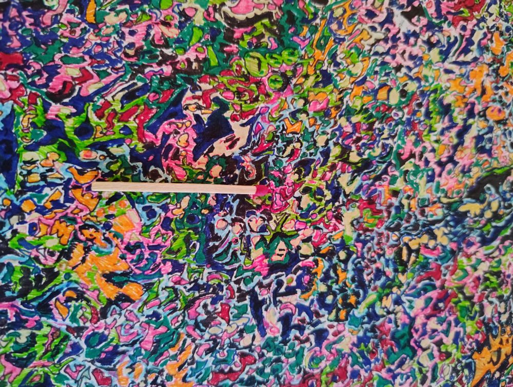 Closeup of "horror vacui" (a fear of empty spaces) style artwork in multicolor abstract. Photo taken with flash, iirc. Random squiggles of color, some outlined, filling a ~10x14" page. Standard kitchen matchstick for scale. 