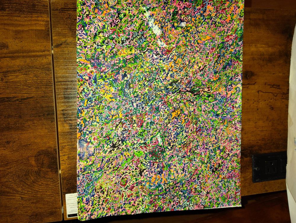 "horror vacui" (a fear of empty spaces) style artwork in multicolor abstract. Photo taken without flash, iirc. Random squiggles of color, some outlined, filling a ~10x14" page. Visible damage in the upper quarter. 