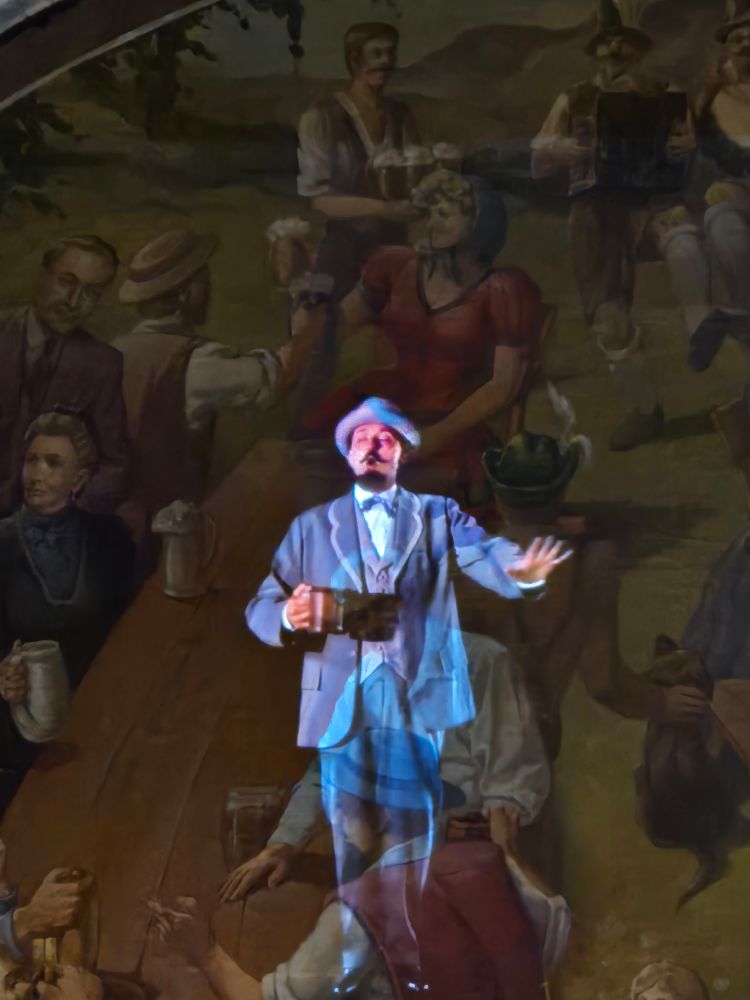 Friedrich Miller himself, wearing a blue suit and matching hat, tells you about his beer while holding a pint against a backdrop of Milwaukee Germans frolicking in a biergarten