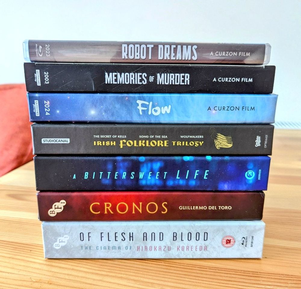 A stack of blu ray boxes: Robot Dreams, Memories of Murder, Flow, The Irish Folklore Trilogy, A Bittersweet Life, Crono, Of Flesh and Blood: The Cinema of Hirokazu Koreeda