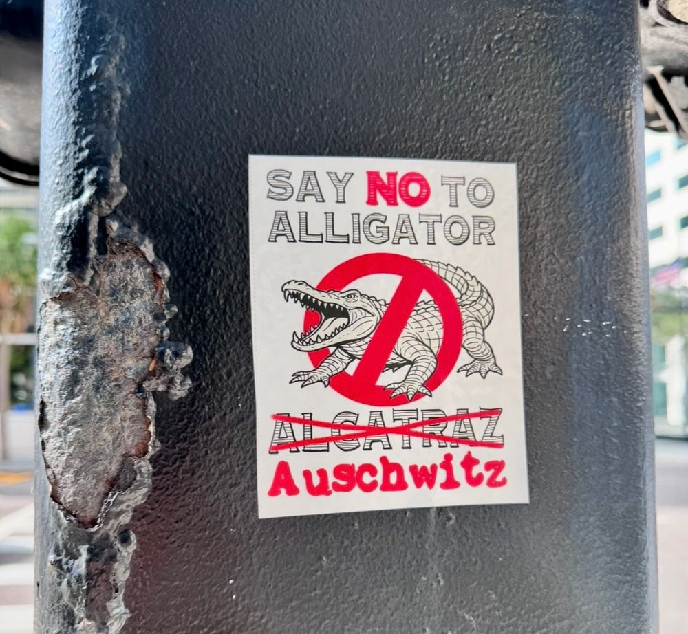 Sticker on pole has a picture of an alligator with a 🚫 over it.

Reads:

SAY NO TO ALLIGATOR
ALCATRAZ