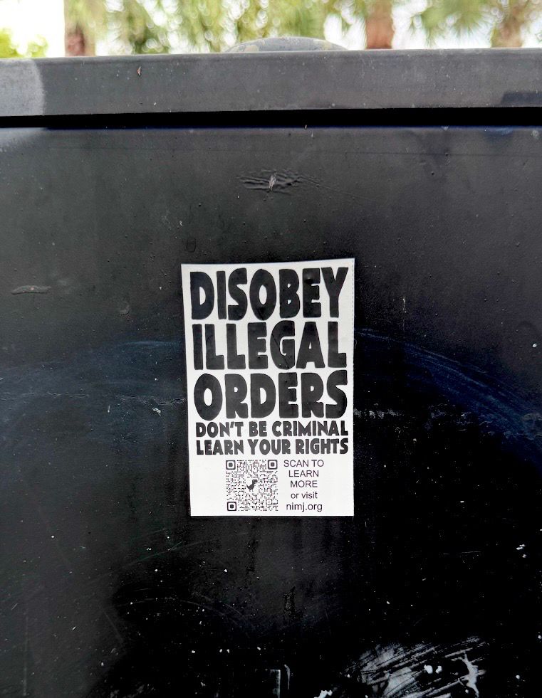 Sticker on a black box reads: DISOBEY ILLEGAL ORDERS DON'T BE CRIMINAL LEARN YOUR RIGHTS SCAN TO LEARN MORE or visit nimj.org