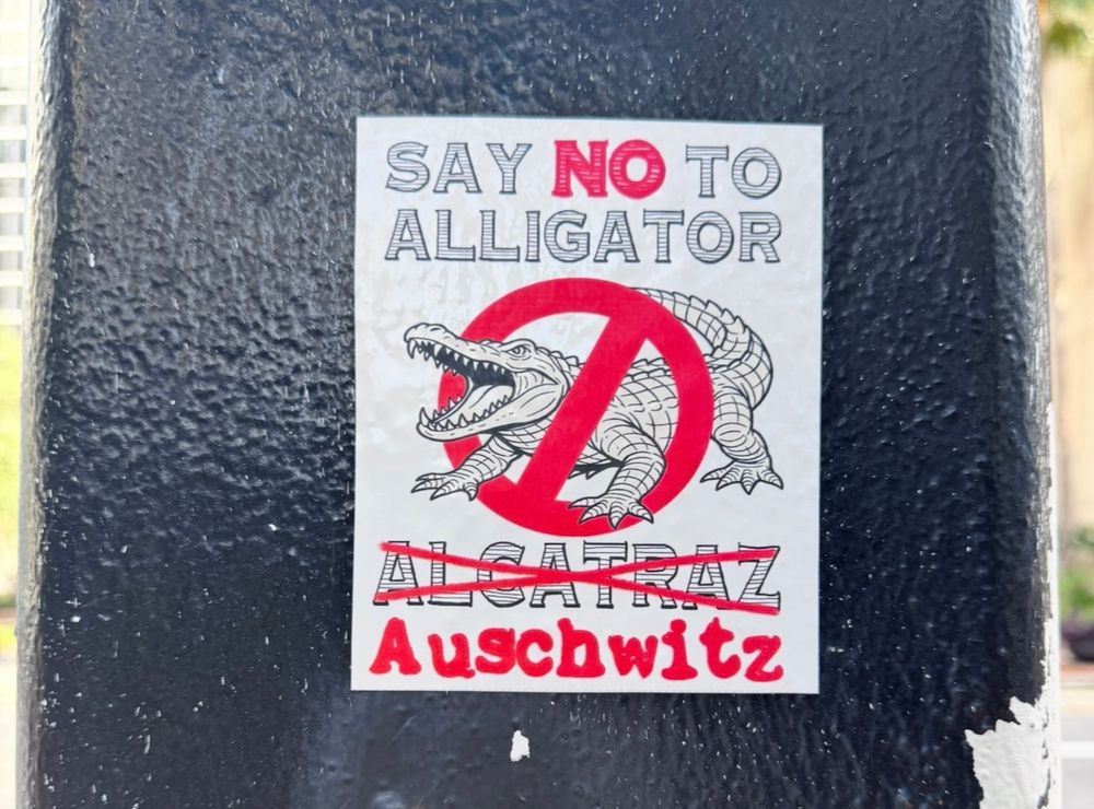 Picture of a sticker on a pole that has an alligator with a 🚫 over it and says:

Say no to alligator Alcatraz.