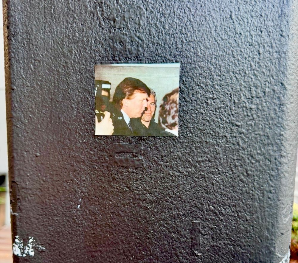 Picture of a sticker on a pole that is a picture of Donald Trump and Jeffrey Epstein.