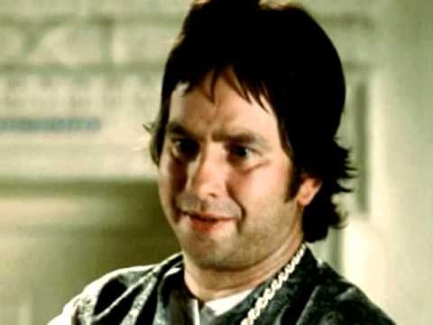 A man with brown hair and a gold chain making a funny face