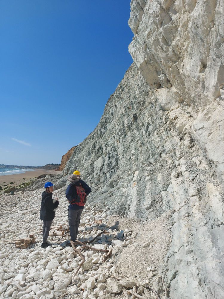 Three people stand talking in front of a cliff made up of distinct bands of light and dark coloured chalk.