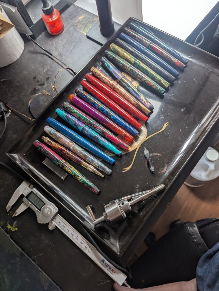 multicolored fountain pens on black tray with tools on black desk 