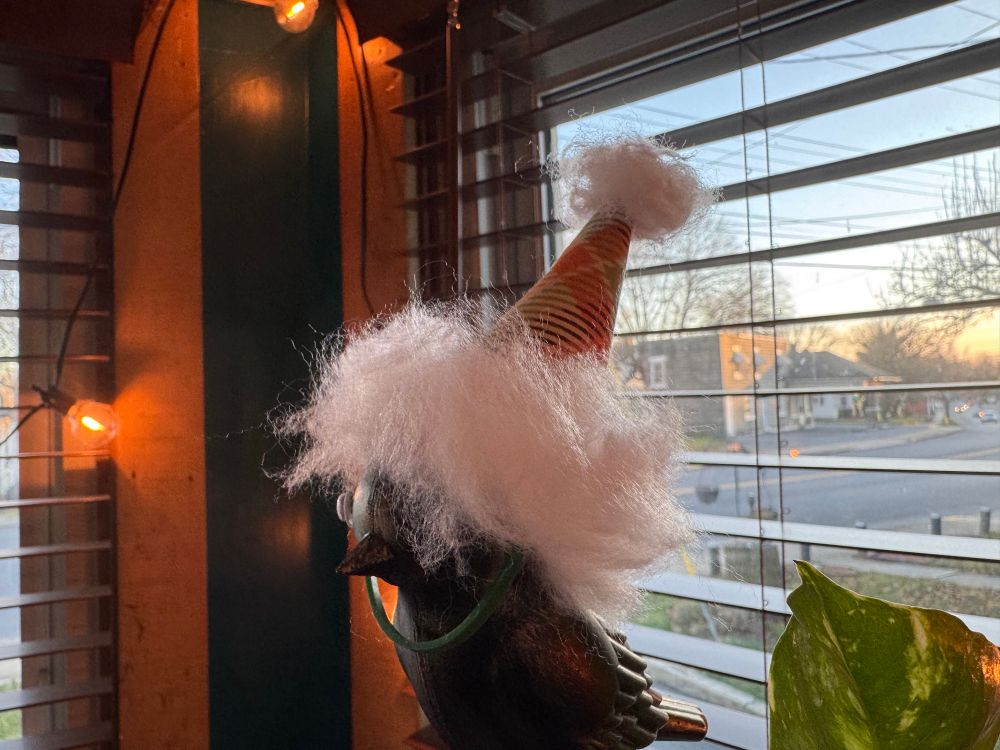 A plastic bird in a window with a makeshift Santa cap on his head.