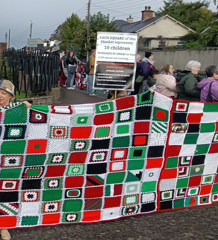 Blanket of many squares, poster says: Each square of this blanket represents 10 children murdered by Israel, 2,300 squares and counting.