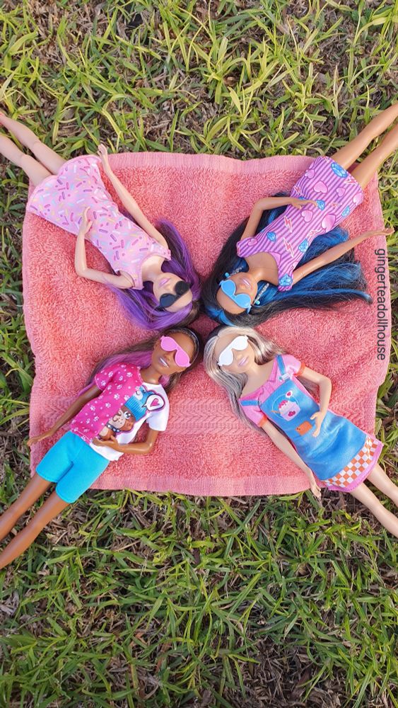 Clockwise from top right: Anna, Joy, Cheri and Skipper. Four teenage girl dolls laying down on an medium orange coloured blanket wearing different coloured aviator sunglasses. Cheri, Anna and Joy dolls belong to the Skipper First Jobs line: Cheri the dog sitter, Anna the ear piercer and Joy the snack bar attendant. Skipper doll is from the 2022 Bounce House playset.