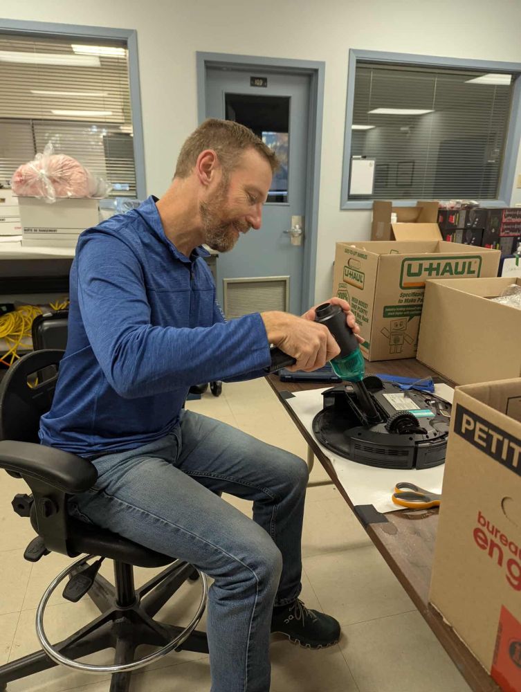 Our Senior Conservator, Ian Loughead sitting is a chair vacuuming a robot vacuum with a small handheld vacuum.