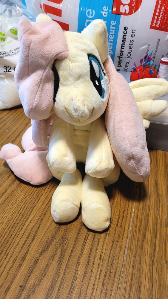 Photo of fluttershy plushie on its front view on a table with my project supplies behind it
Fluttershy is a pink haired and yellow Pegasus pony in MLP