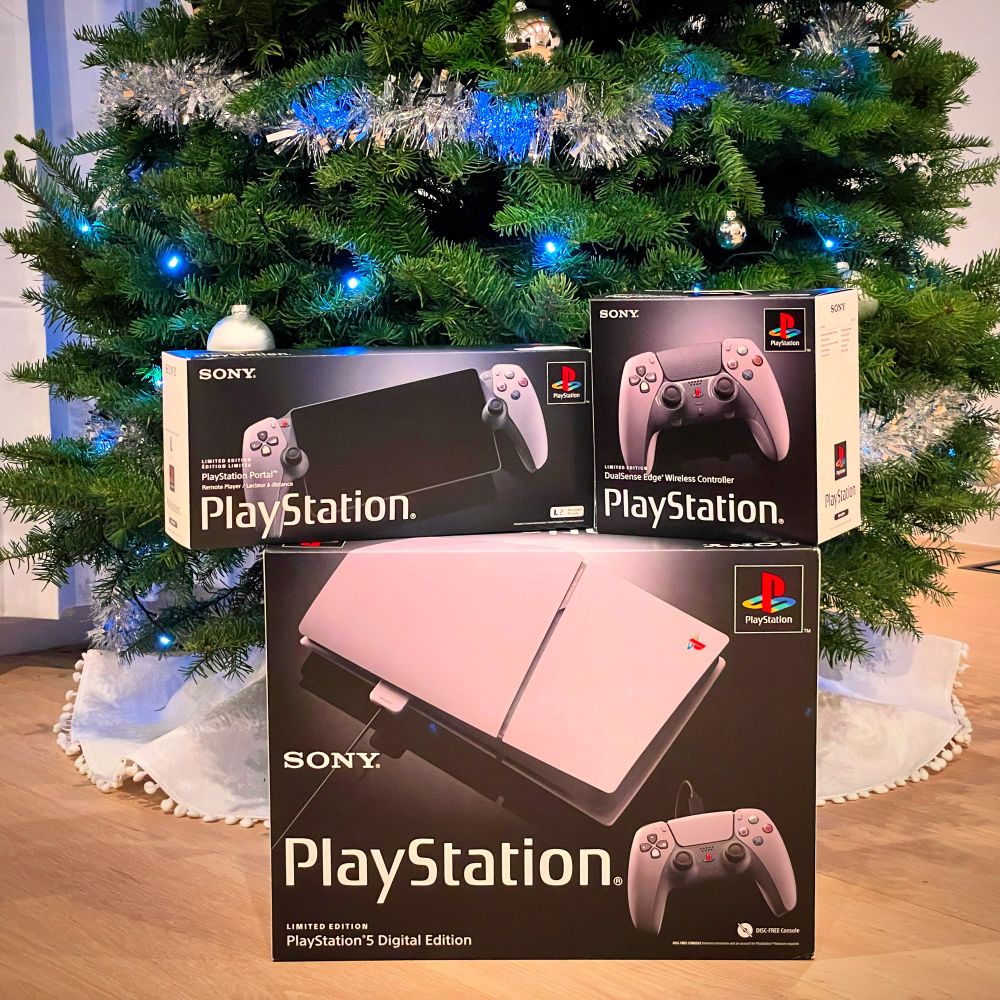 Unopened PS5 Slim, PlayStation Portal, and DualSense Edge, all 30th anniversary edition, under a Christmas tree.