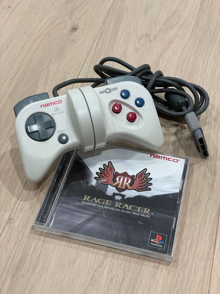Rage Racer for the original PlayStation console in its jewel case, sitting casually with an original Namco NeGCon PS1 controller.