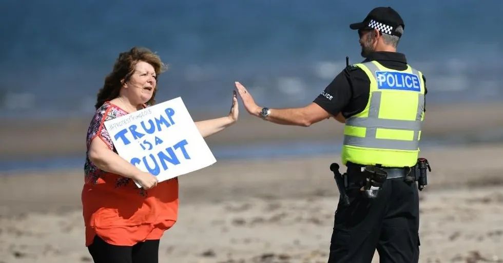 A woman holding a placard saying "Trump is a cunt" and getting a high five from a Scottish police officer.