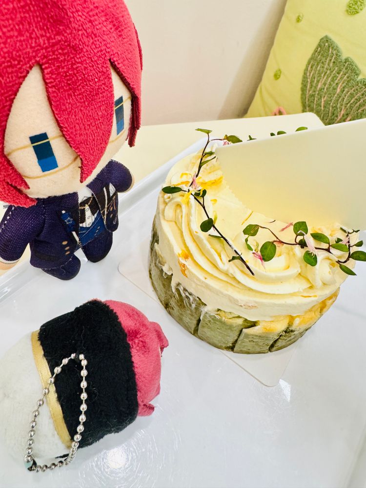 Photo of Ibara nui and Ibara screen wiper nui sitting around a cake I bought today. It’s a matcha and grapefruit cake with leaves and flower petals on it. A cake knife is cutting it 
