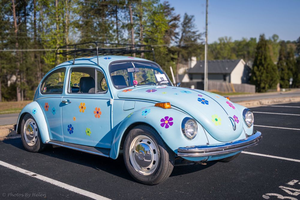 The pale blue 1971 VW beetle sits quietly in the morning sun, waiting for the car show to start.  He’s covered in brightly colored flower magnets.  
