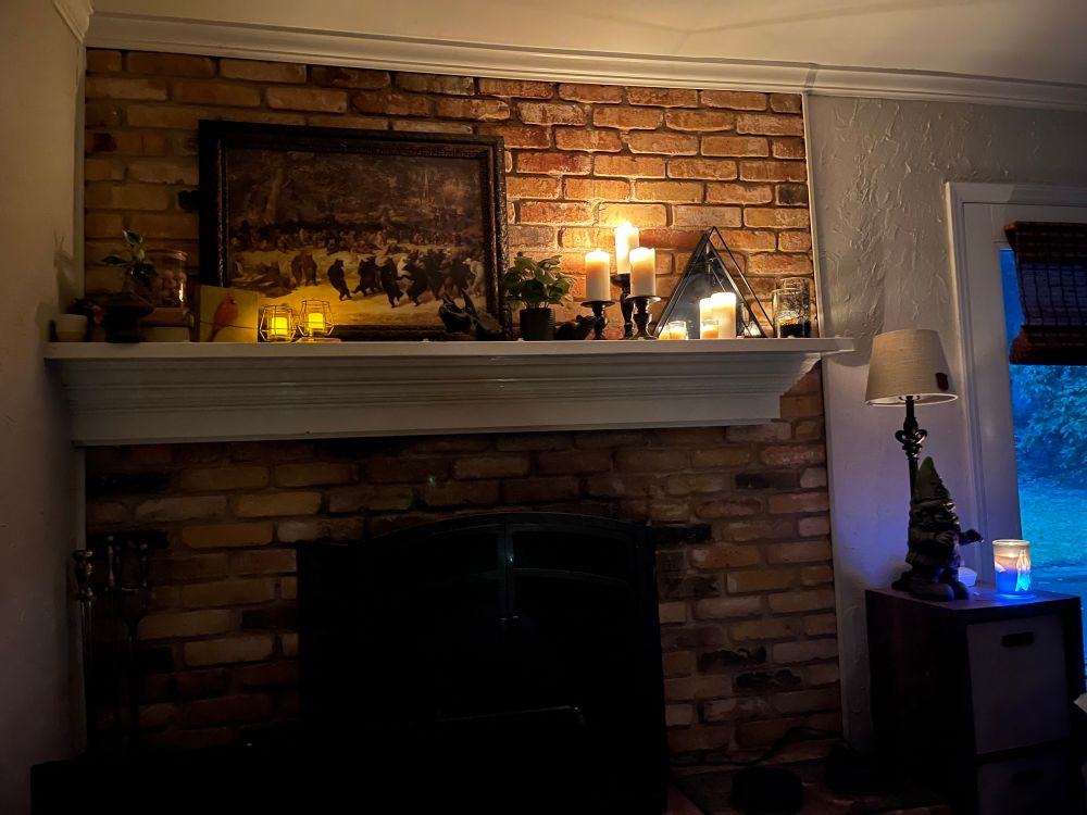 Various candles on a white mantle hanging on a brick fireplace