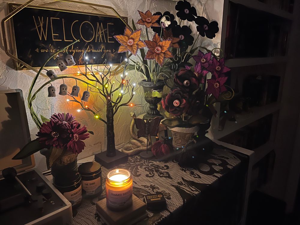 A lit Cowboy & Cricket candle set in front of a small decorative tree with Halloween lights, surrounded by other floral Halloween decor