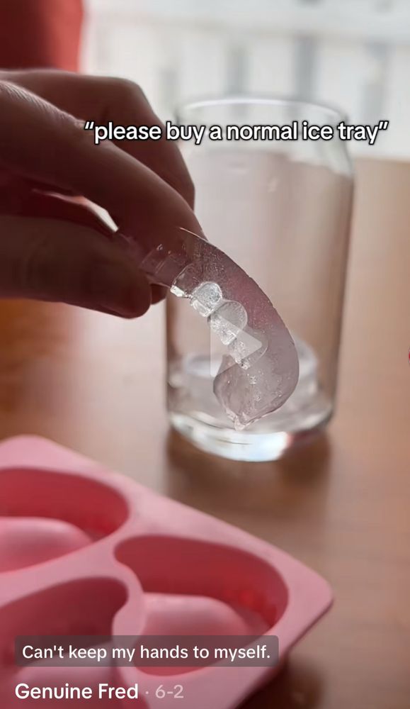 A hand holding what looks like dentures made of ice over a pink silicone ice tray molded to produce ice shaped like teeth