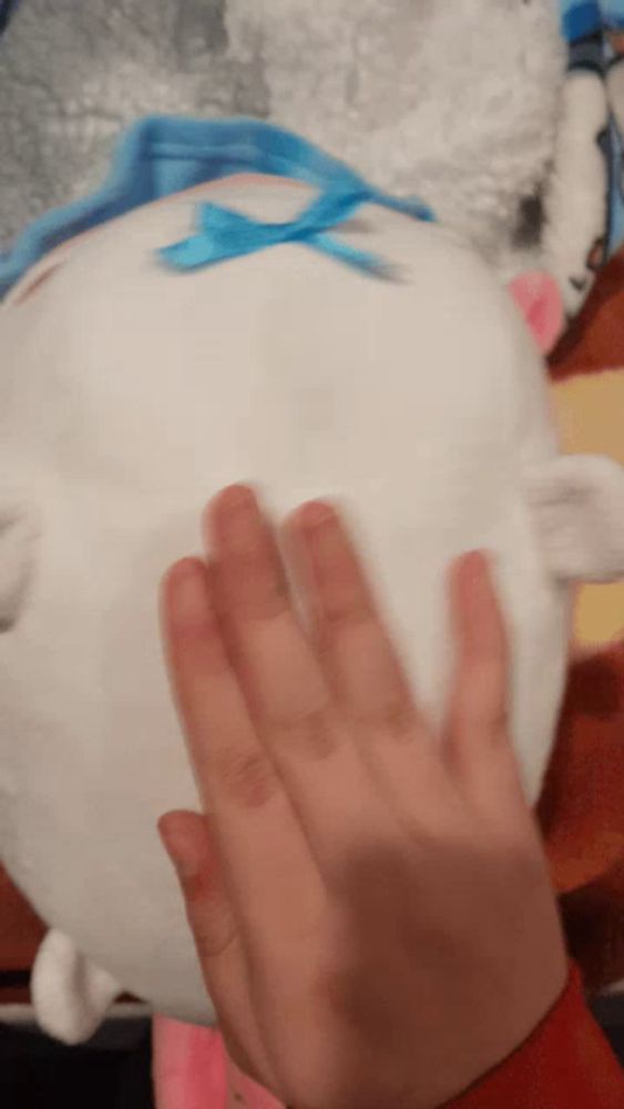 a person 's hand is touching a stuffed animal with a blue bow on it