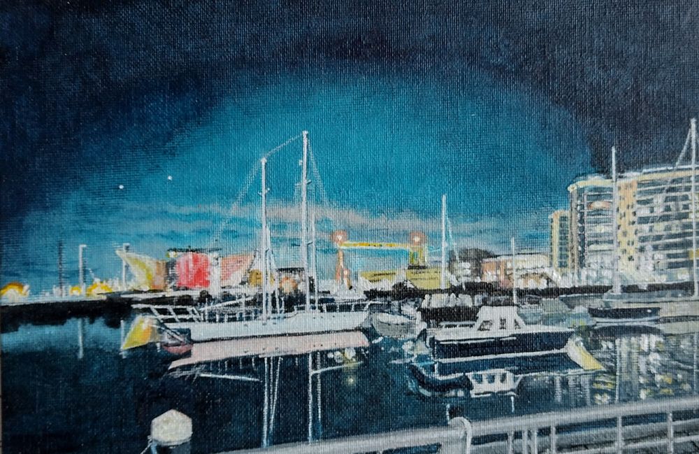 Painting of a night sky lit by the bright lights of a dockyard.  There are buildings in the background, boats and water in the foreground.  The water is calm and almost still.