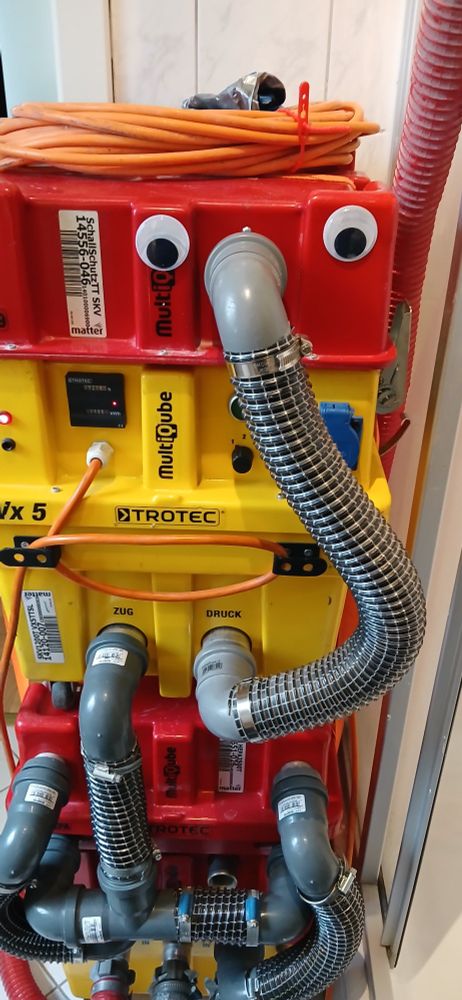 trocknungsgerät vor fliesenwand, gelbe und rote elemente mit verschiedenen grauen "rüsseln"(schläuchen). ganz oben 2 4cm-wackelaugen, dazwischen der oberste rüssel.