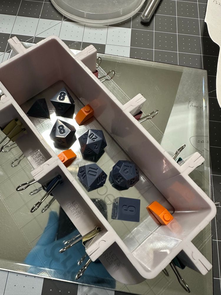 A set of polyhedral dice and a few LEGO pieces, in a box to be filled with silicone