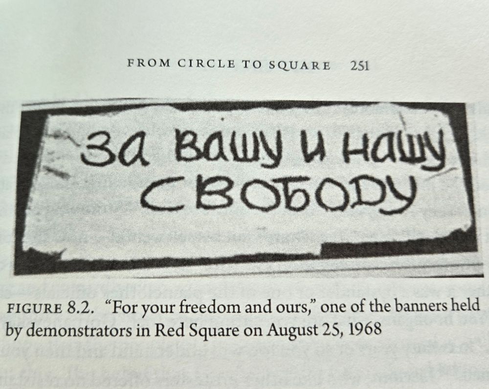 Black and white photo of a banner that reads "For your freedom and ours" in Russian. Text reads that it was one of the banners held by demonstrators in Red Square on August 25, 1968