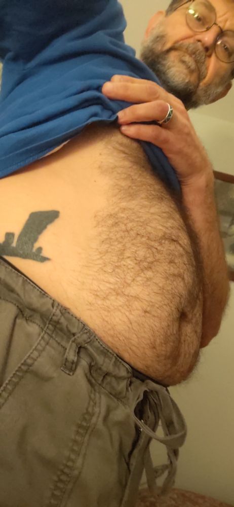 Oblique selfie showing me from hip to forehead. I've pulled up my shirt and the side of my furry belly is visible. Part of my tattoo of the Stones of Stennis is showing on my side. 