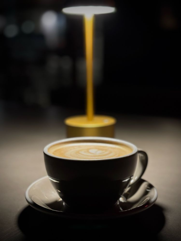 A well-lit latte at an outdoor table at night 