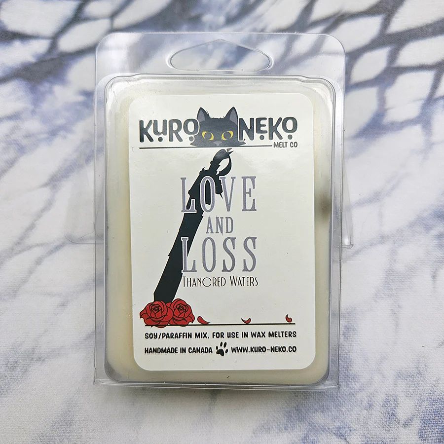 A set of wax melts in a clamshell on a blue and white tie dye background. The pictured scent is Love and Loss: Thancred Waters.