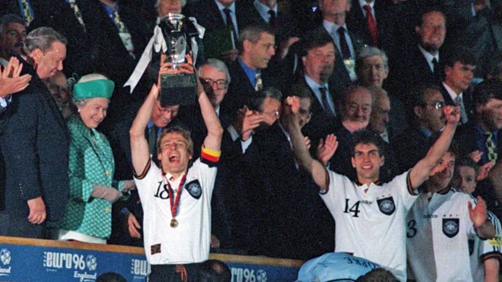Klinsmann hält den Europameister-Pokal neben der Queen im Jahr 1996 hoch.