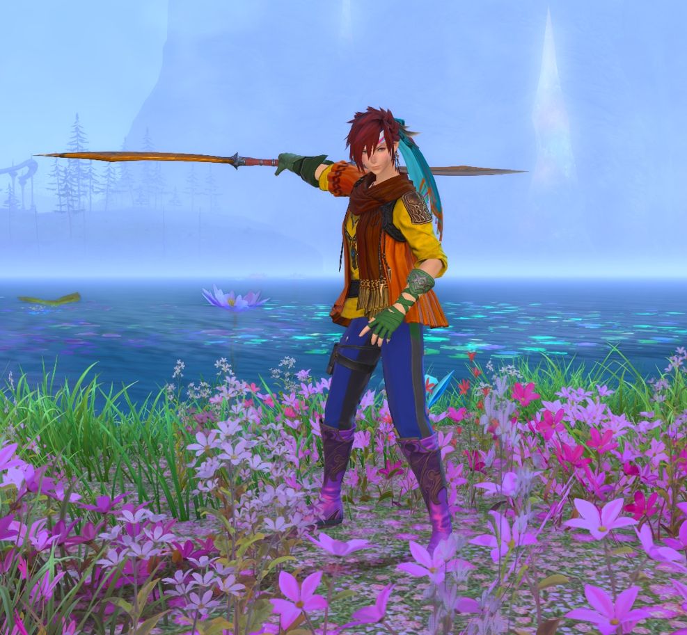 A screenshot of my WOL in Il Mheg. She is wearing gear that is dyed in the rainbow colors from top to bottom: Red spiky hair, orange scarf and overshirt, yellow shirt, green elbow-length arm protectors, blue and black pants and purple high boots. She also wears a Ribbon-headband in pale blue, pink and white. She is standing in fron of the big lake in Il Mheg in a field of pink flowers. She hhas her right arm stretched out behind her, holding her Viper-blade horizontally. The blue lake has water flowers floating on it and in the distance several trees and a waterfall can be seen through the fog.